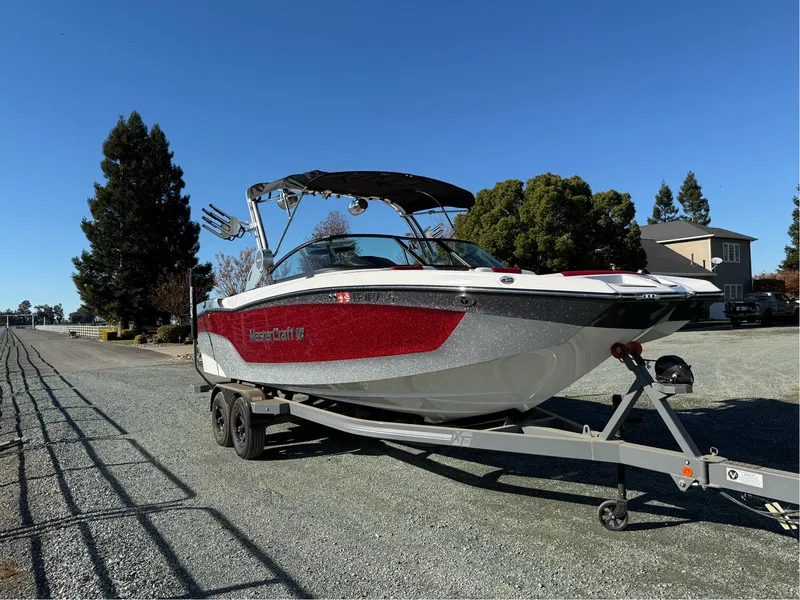 Slide: The Image of 2022 MasterCraft XT24 boat on trailer, parked outdoors under clear blue sky. - 3