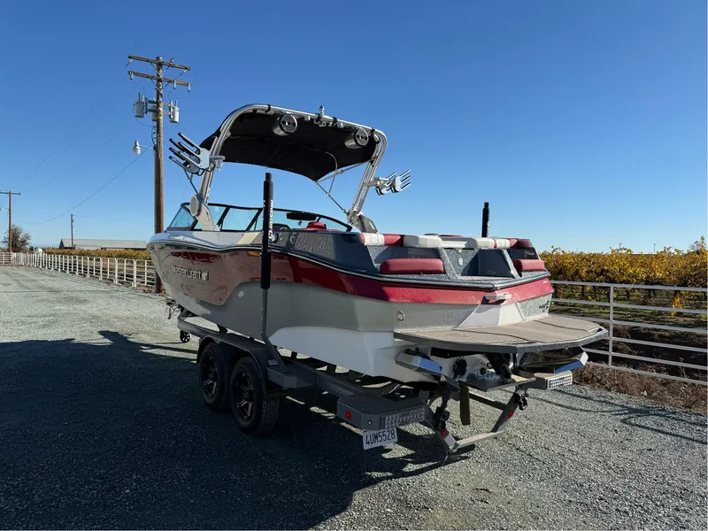 Slide: The Image of 2022 MasterCraft XT24 boat on trailer, parked on gravel road under clear blue sky. - 7