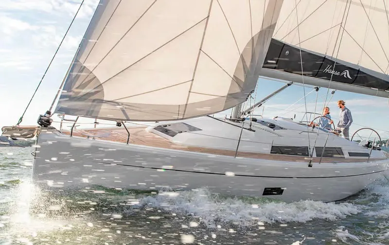 Slide: The Image of 2019 Hanse 348 sailboat navigating through waves with full sails and two people onboard. - 8