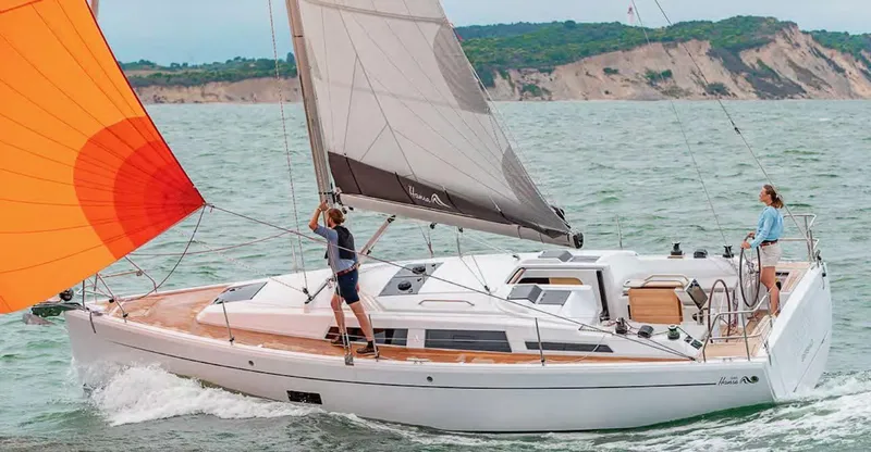 Slide: The Image of 2019 Hanse 348 sailboat navigating coastal waters with vibrant sails and crew on deck. - 9