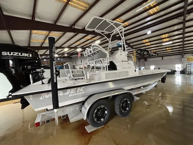 Slide: The Image of 2025 Majek 24 Reaper boat in showroom, featuring Suzuki engine and dual-axle trailer. - 2