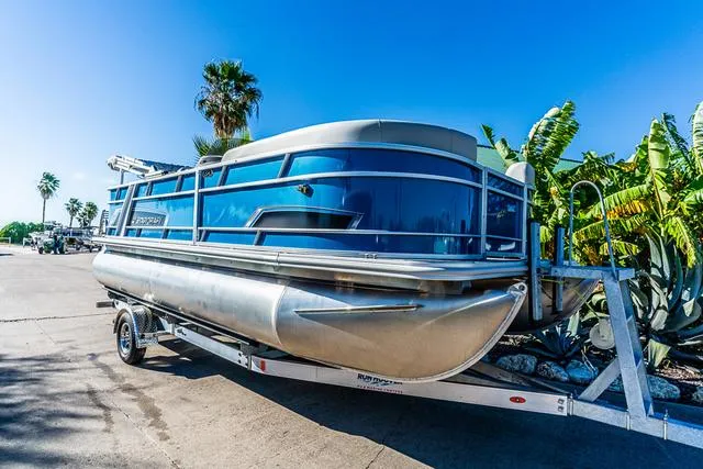Slide: The Image of 2025 Starcraft EX20FD pontoon boat on trailer, surrounded by palm trees under clear blue sky. - 6