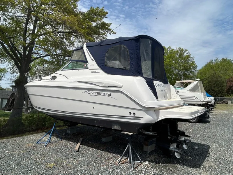 Slide: The Image of 2003 Monterey 302 Cruiser boat on stands, white hull, blue canopy, outdoor setting. - 2