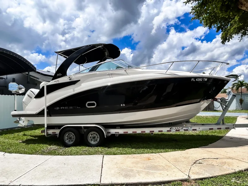 The Image of 2023 Regal 26 XO boat on trailer, black and white design, parked outdoors under cloudy sky. - 0