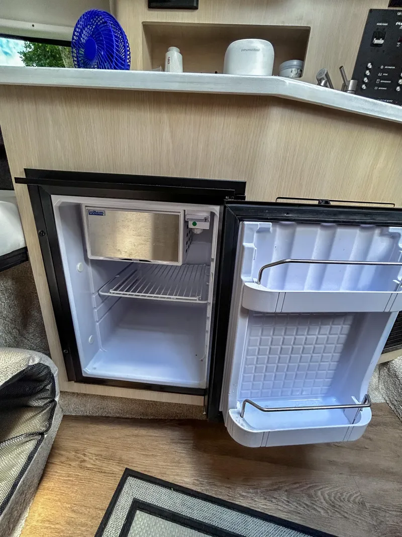 Slide: The Image of 2023 Regal 26 XO boat interior with open mini fridge, wooden cabinetry, and countertop. - 13