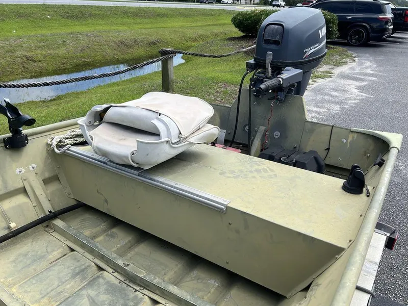 Slide: The Image of 1989 Polar Kraft 15' Jon boat with outboard motor and seating, parked near a grassy area. - 11