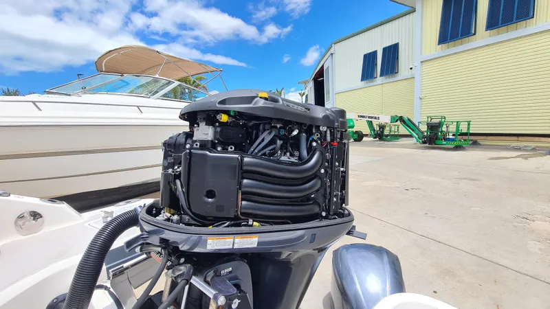 Slide: The Image of 2018 Chaparral Suncoast 250 Deluxe boat engine exposed, docked near a warehouse under blue sky. - 38