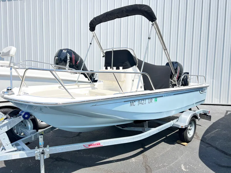 Slide: The Image of 2022 Boston Whaler 150 Montauk boat on trailer with canopy, parked outdoors. - 4