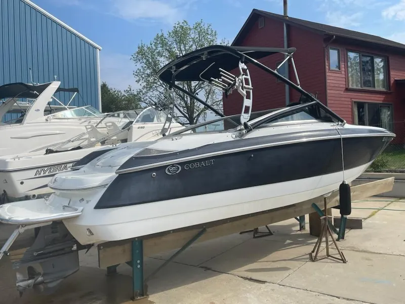 Slide: The Image of 2005 Cobalt 246 boat on a trailer, parked near a red building and blue warehouse. - 2