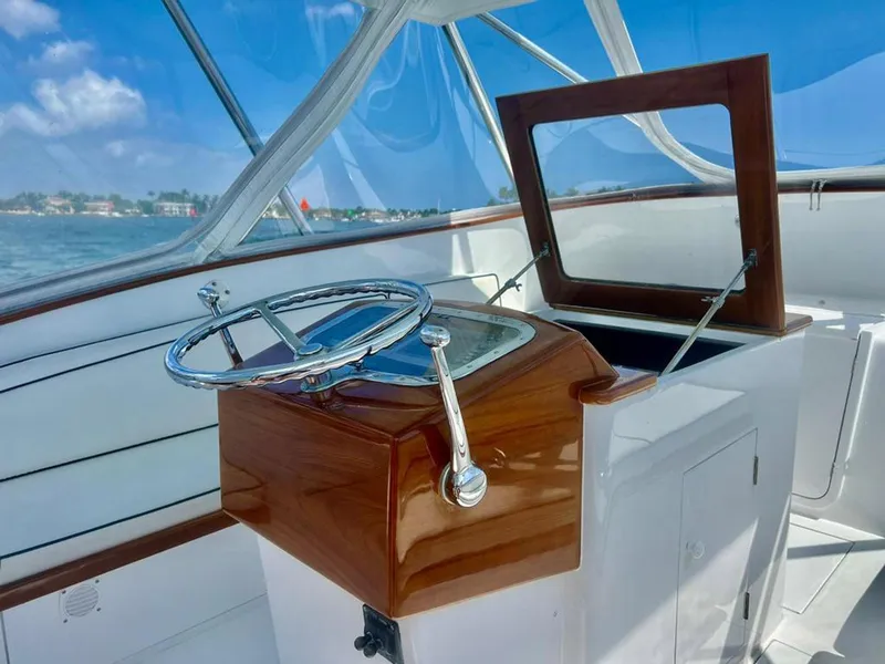 Slide: The Image of 1999 Gamefisherman 34 Express helm with wooden accents and open hatch, under clear blue skies. - 7