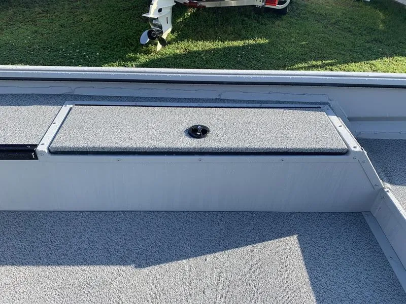 Slide: The Image of 2025 SeaArk DXS 1548 DKLD boat interior with storage compartment, gray carpet, and outdoor setting. - 12