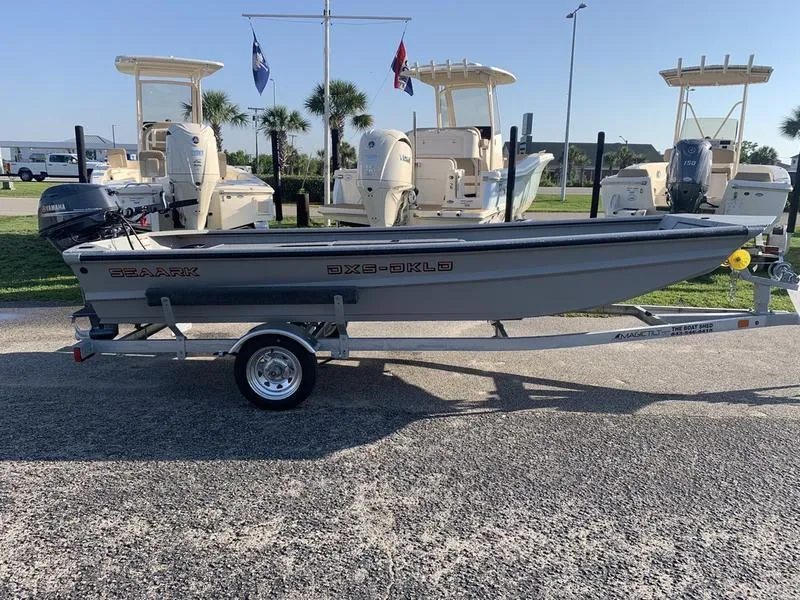 Slide: The Image of 2025 SeaArk DXS 1548 DKLD boat on trailer, parked outdoors with other boats. - 5