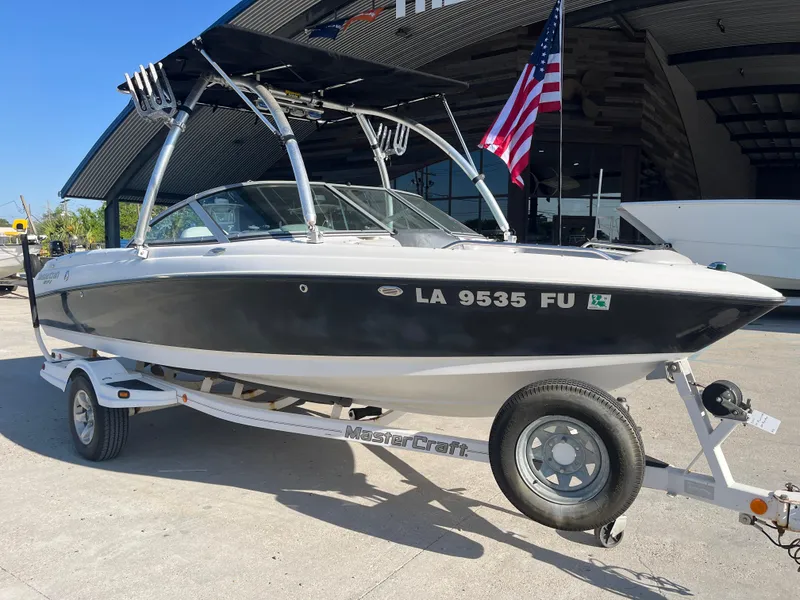 Slide: The Image of 2004 MasterCraft 210 Maristar boat on trailer, parked outdoors with American flag. - 2