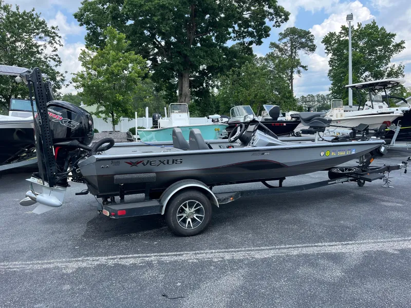 Slide: The Image of 2022 Vexus AVX189 boat on trailer, parked outdoors with trees and other boats nearby. - 4