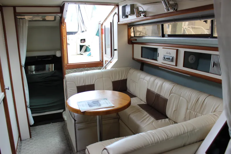 Slide: The Image of 1988 Sea Ray 340 Sundancer interior with beige seating, wooden table, and windows. - 24