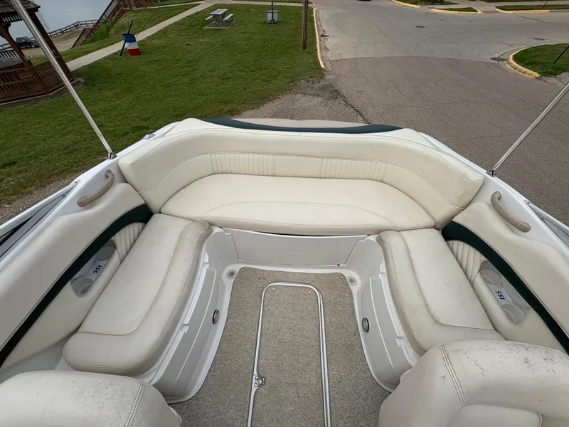 Slide: The Image of 1999 Chris-Craft 210 Bowrider with white seating, docked near a grassy area and road. - 23