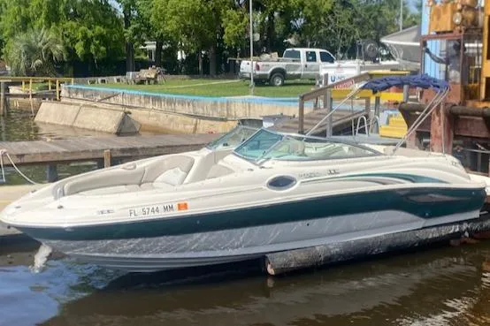 Slide: The Image of 2004 Sea Ray 240 Sundeck boat docked by the water, with trees and vehicles in the background. - 4