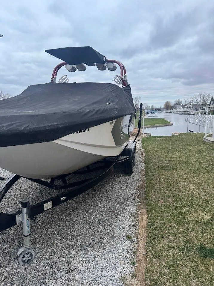 Slide: The Image of 2013 Nautique Super Air G23 boat covered, parked on gravel near a lake. - 22