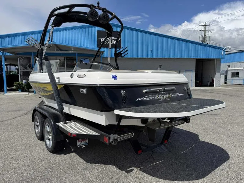 Slide: The Image of 2006 Tigé 21i boat on trailer, parked outside a blue building under a cloudy sky. - 6