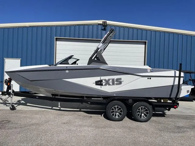 Slide: The Image of 2024 Axis Wake Research T220-R boat on trailer, parked outside blue building. - 1