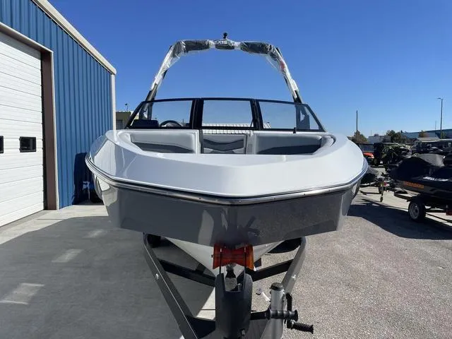 Slide: The Image of 2024 Axis Wake Research T220-R boat, front view, parked outdoors near a blue building. - 3