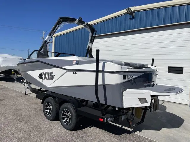 Slide: The Image of 2024 Axis Wake Research T220-R boat on trailer, parked near a blue building. - 8