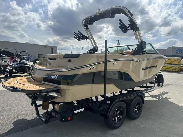 Slide: The Image of 2024 MasterCraft NXT21 boat on trailer, beige and black design, under cloudy sky. - 6