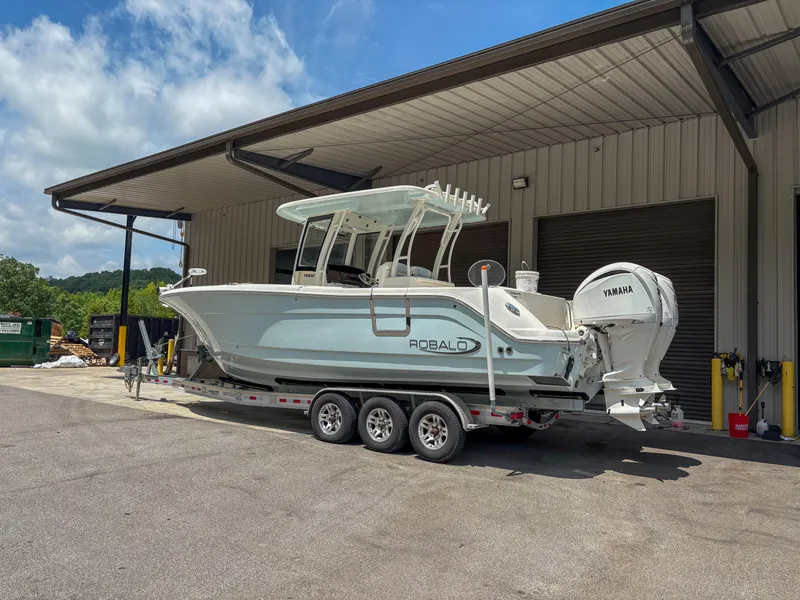 Slide: The Image of 2023 Robalo R302 boat on trailer, parked outside a building under a clear sky. - 1