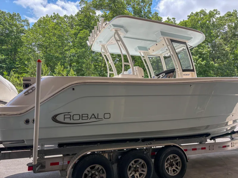 Slide: The Image of 2023 Robalo R302 boat on trailer, parked outdoors with trees in the background. - 4