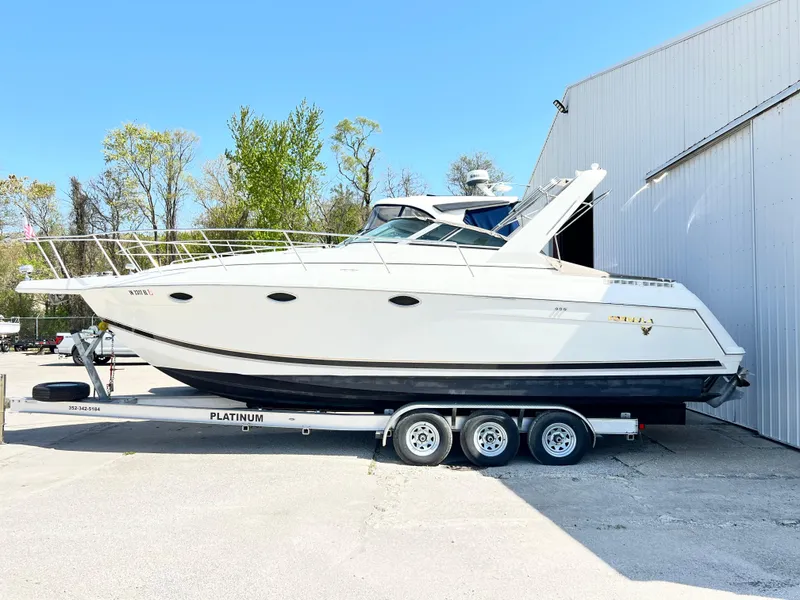 Slide: The Image of 1999 Formula 31 PC boat on trailer, parked near a building, under clear blue sky. - 2