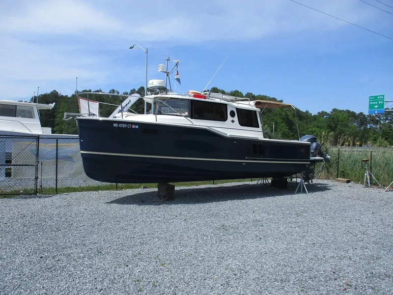 Slide: The Image of 2020 Ranger Tugs R-27 LE boat on gravel lot, surrounded by fence and trees. - 1