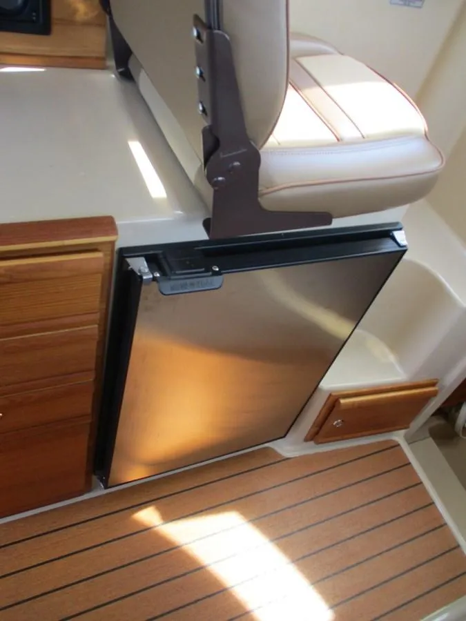 Slide: The Image of 2020 Ranger Tugs R-27 LE interior with compact stainless steel fridge and wooden flooring. - 15