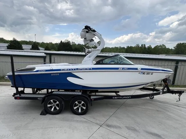 Slide: The Image of 2014 Centurion Enzo SS210 boat on trailer, blue and white design, parked outdoors. - 1