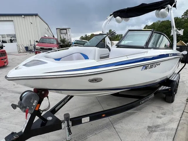 Slide: The Image of 2014 Centurion Enzo SS210 boat on trailer, white with blue accents, parked outdoors. - 13