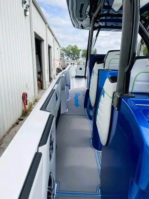 Slide: The Image of 2025 Renegade 38 Open boat interior with blue and white seating, docked near a warehouse. - 12