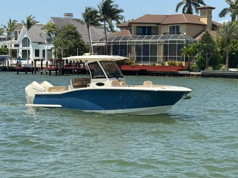 Slide: The Image of 2023 Scout 277 LXF boat cruising on a sunny waterfront with luxury homes in the background. - 1