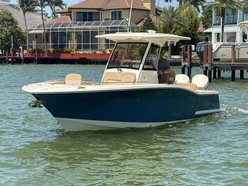 Slide: The Image of 2023 Scout 277 LXF boat cruising on a sunny waterfront with houses in the background. - 2