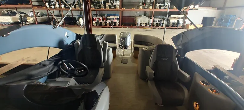 Slide: The Image of 2021 Bennington RX 25 RXFBA pontoon boat interior with seating and steering wheel in a storage facility. - 17