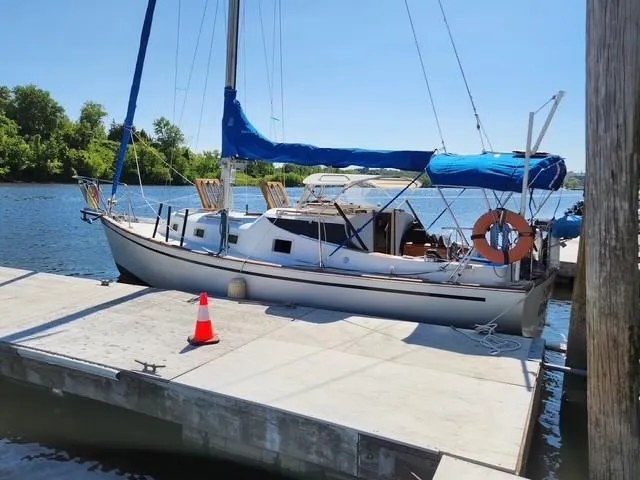 Slide: The Image of 1977 Bombay Express sailboat docked on a sunny day with blue sails and life preserver. - 4