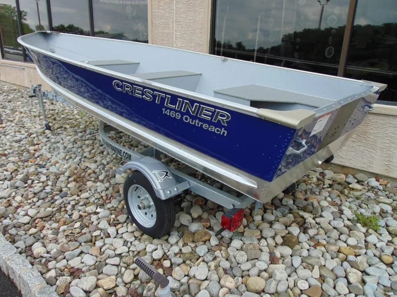 Slide: The Image of 2024 Crestliner 1469 Outreach boat on trailer, displayed outdoors on rocky surface. - 3