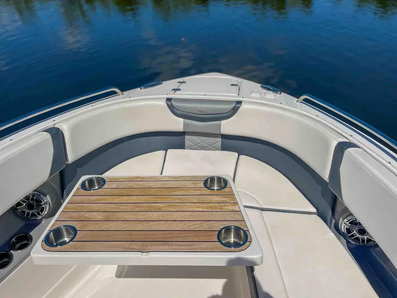 Slide: The Image of 2021 Chaparral 300 OSX boat interior with cushioned seating and wooden table on calm water. - 24