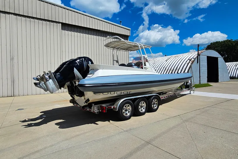 Slide: The Image of 2012 Cougar R10 Rigid Inflatable boat on trailer, parked near industrial building. - 2