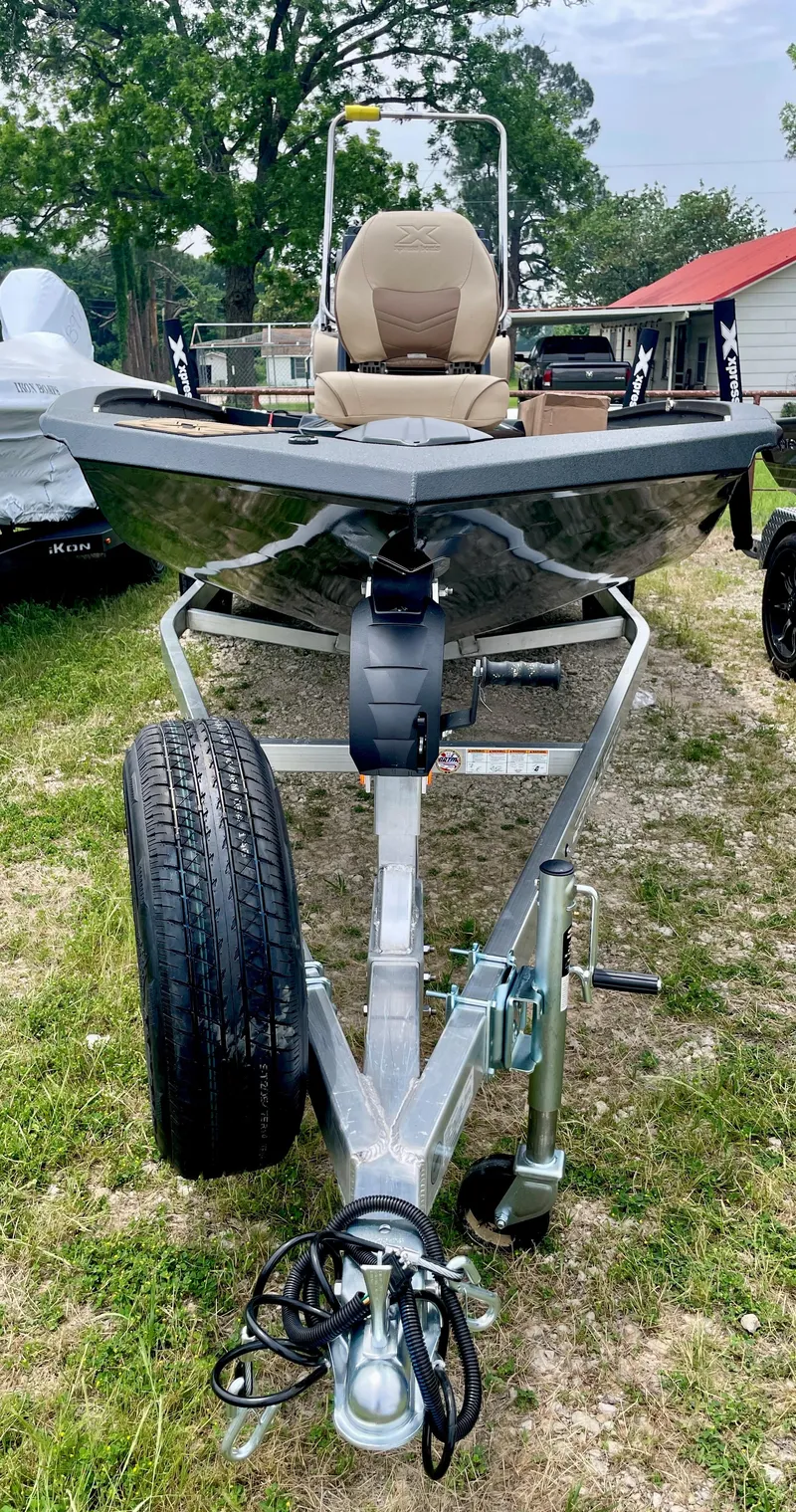 Slide: The Image of 2025 Xpress H20B boat on trailer, parked on grass, with trees and buildings in background. - 10