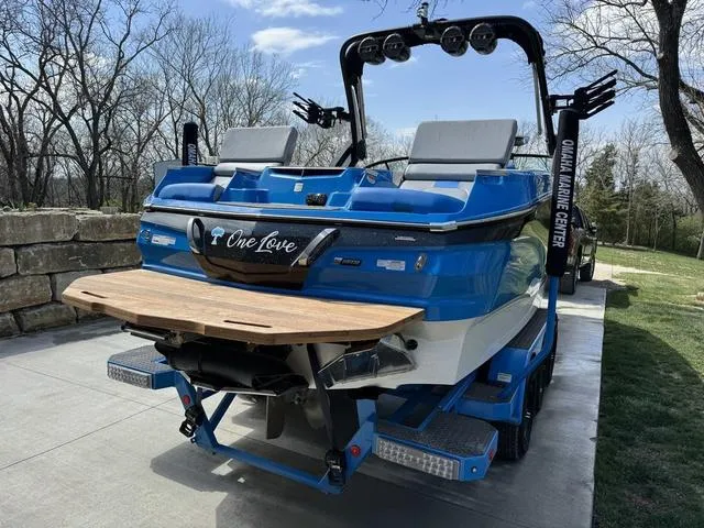 Slide: The Image of 2022 MasterCraft X24 boat with blue exterior and wooden swim platform, parked on concrete driveway. - 6