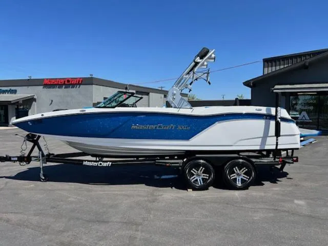 Slide: The Image of 2018 MasterCraft NXT22 boat on trailer, parked outdoors under clear blue sky. - 1
