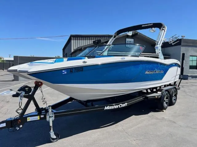 Slide: The Image of 2018 MasterCraft NXT22 boat on trailer, blue and white design, parked outdoors. - 2