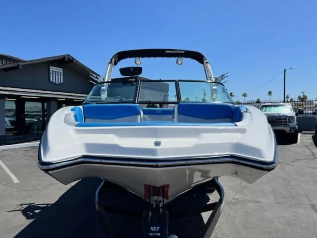 Slide: The Image of 2018 MasterCraft NXT22 boat with blue seating, parked outdoors under clear sky. - 3