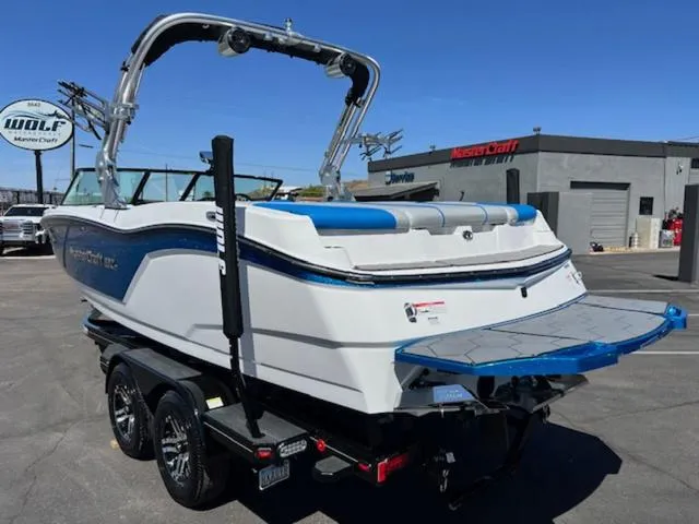 Slide: The Image of 2018 MasterCraft NXT22 boat on trailer, displayed at dealership under clear blue sky. - 8