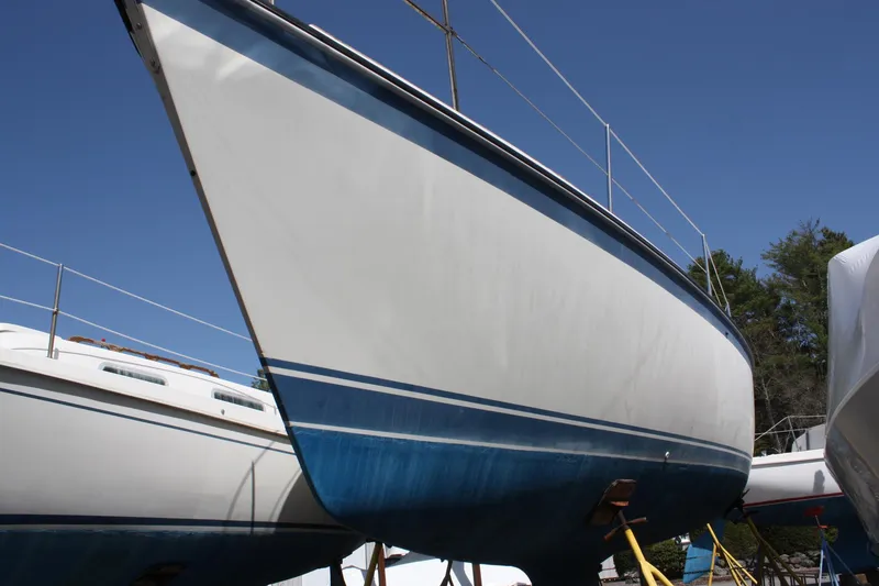 The Image of 1981 O'Day 34 sailboat on land, white hull with blue bottom, clear sky background. - 0