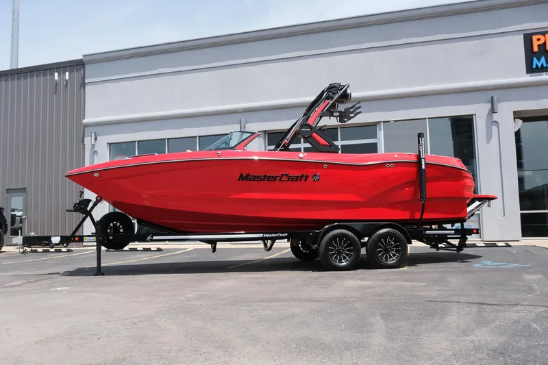 Slide: The Image of 2025 MasterCraft X24 boat in vibrant red on a trailer outside a building. - 2